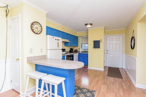 Una cocina con armarios azules, un refrigerador blanco y un reloj en la pared.