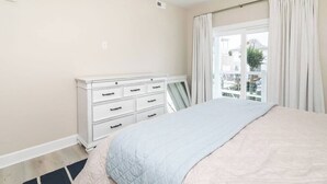 A bedroom with a bed, a dresser, a window with curtains, and a view of the outside.