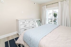 A bedroom with a bed, a dresser, a window with curtains, and a view of the outside.