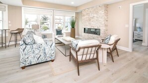 A spacious living area with a sofa, a dining table, and chairs. There is a stone fireplace and a TV mounted on the wall.