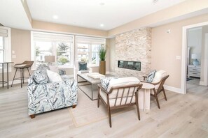 A spacious living area with a sofa, a dining table, and chairs. There is a stone fireplace and a TV mounted on the wall.