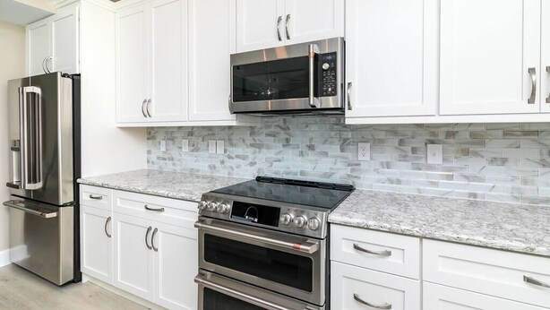 A kitchen with white cabinets, a stainless steel refrigerator, a microwave, and a double oven.