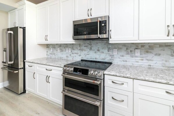 A kitchen with white cabinets, a stainless steel refrigerator, a microwave, and a double oven.