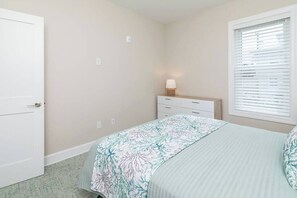 A bedroom with a bed, a nightstand with a lamp, a window with blinds, and a door. - Bayside Splendor - 3BR, 3BA/ boat slip (Ocean City)