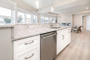 A modern kitchen with a marble countertop, stainless steel dishwasher, and white cabinetry.