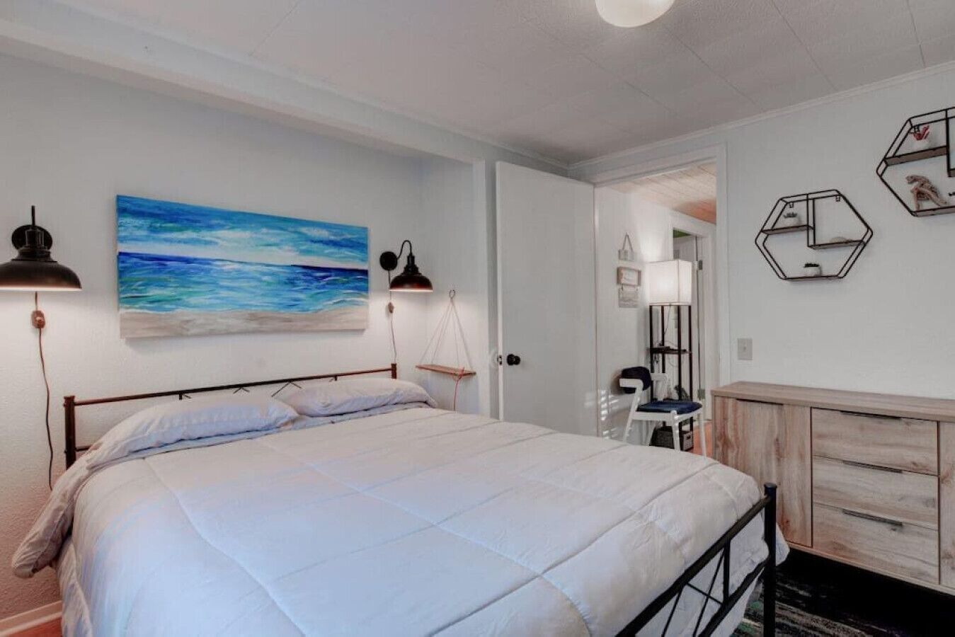 Une chambre à coucher avec un lit, deux lampes fixées au mur, un tableau, une armoire en bois et un miroir.