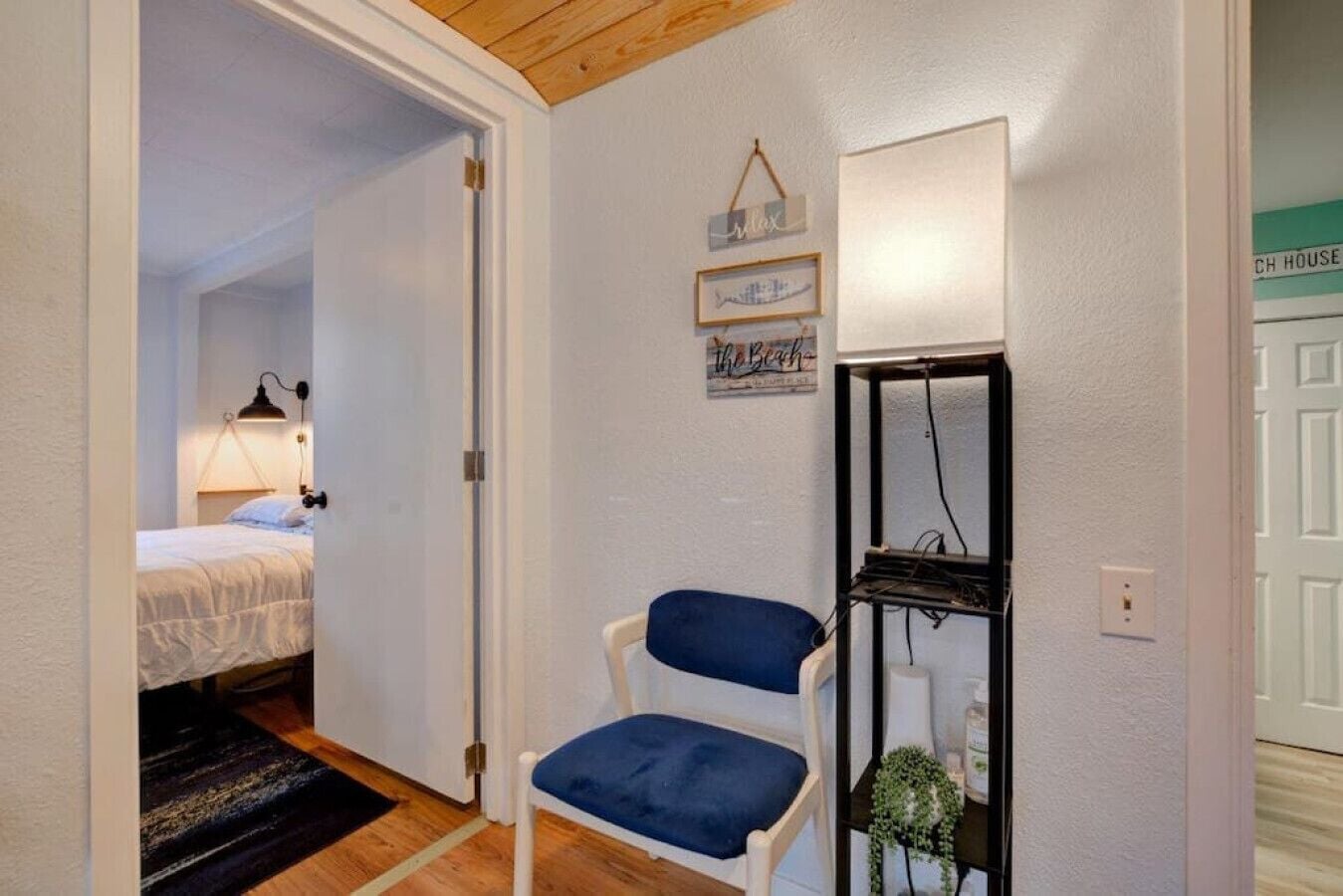 Ein Schlafzimmer mit einem Bett, einem Sessel, einem Regal mit Gegenständen und einer Tür zu einem anderen Raum.