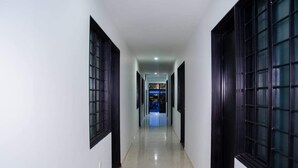 Un pasillo con paredes blancas y puertas de madera oscura que conduce a una habitación con luz azulada.