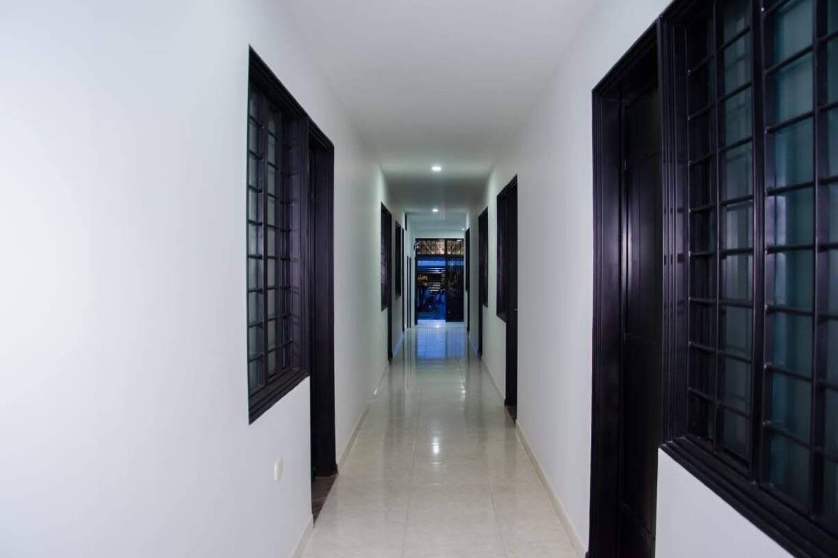 A corridor with white walls and dark wooden doors, leading to a room with a blue-lit interior.