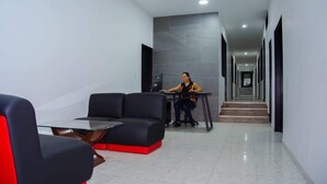 Un moderno vestíbulo de hotel con una mesa de vidrio, sofás negros y una persona trabajando en un escritorio.