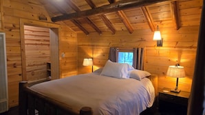 A wooden cabin bedroom with a bed, two bedside lamps, a window with curtains, and a wooden ceiling. - Yuba River Inn (Sierra City)