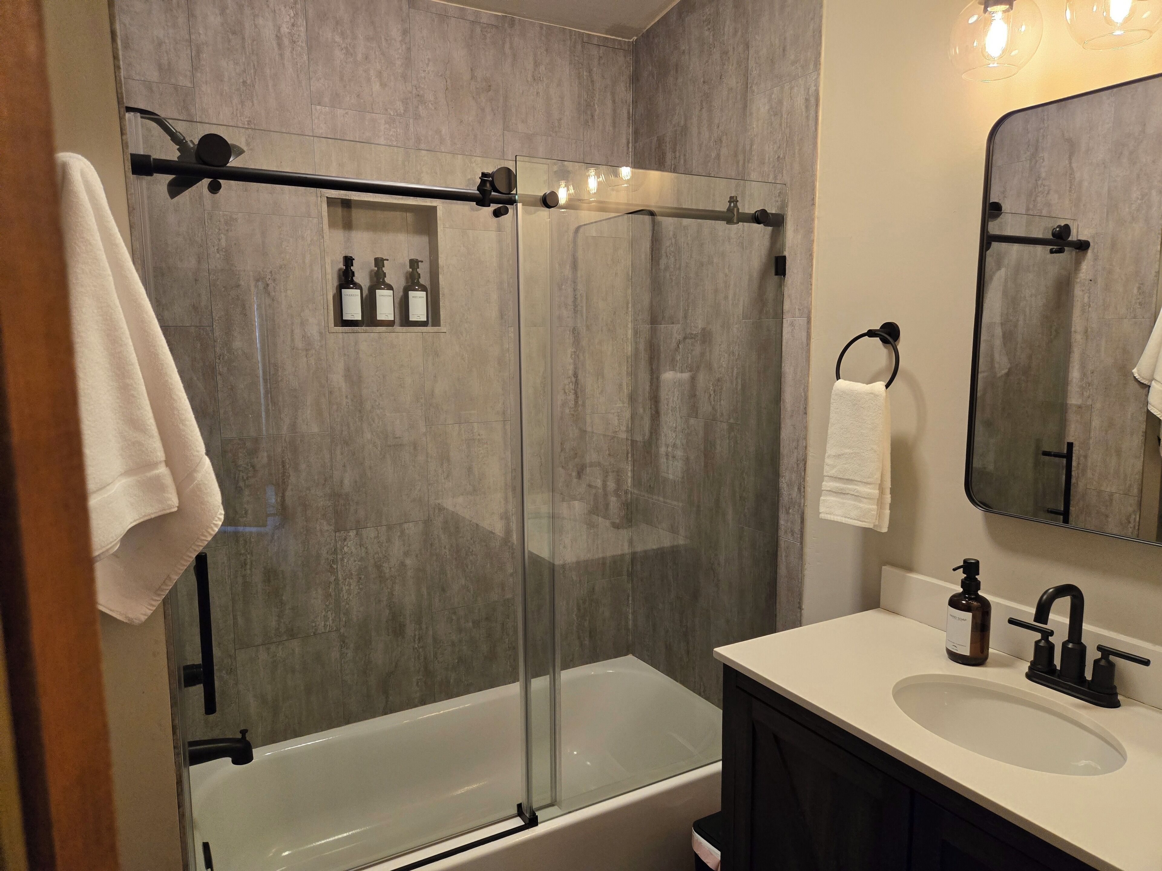 A modern bathroom with a glass-enclosed shower, a white bathtub, and a vanity with a sink and mirror.