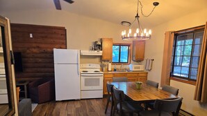 A compact kitchen with wooden cabinets, a white refrigerator, a stove, and a dining table with chairs. - Yuba River Inn (Sierra City)