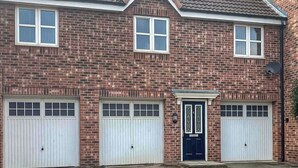 A two-story brick house with a gabled roof, two garage doors, and a front door with a small porch. - The Gainsborough Mews (Gainsborough)