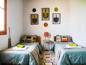 Ein Schlafzimmer mit zwei Betten, Holzboden, einem Fenster und Wanddekorationen, darunter gerahmte Bilder und eine Uhr.