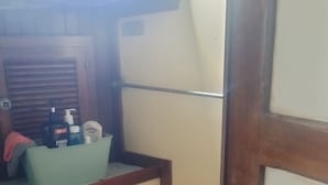 A compact bathroom with a toilet, a small sink, and a mirror. There is a window above the sink, and a wooden cabinet below it. - sailboat on the bay ,close to South Beach and Winwood. (Miami)