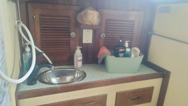 A compact kitchenette with a stainless steel sink, a white bottle, a power stick, and a green container. - sailboat on the bay ,close to South Beach and Winwood. (Miami)