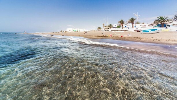 Ein Strand mit klarem Wasser, weißen Gebäuden und Palmen.