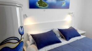 Ein Hotelzimmer mit Bett, zwei Kissen, einem Nachttisch und einem Bild von Inseln an der Wand.