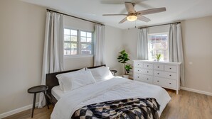 Une chambre à coucher avec un lit, un ventilateur de plafond, une commode, une fenêtre avec des rideaux et une plante en pot.