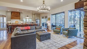 Un vaste espace de vie comprenant un grand canapé, un pouf et deux fauteuils. On aperçoit à l’arrière-plan un coin repas avec une table et des chaises en bois.