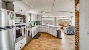 A modern kitchen with white cabinetry, stainless steel appliances, and a wooden floor.