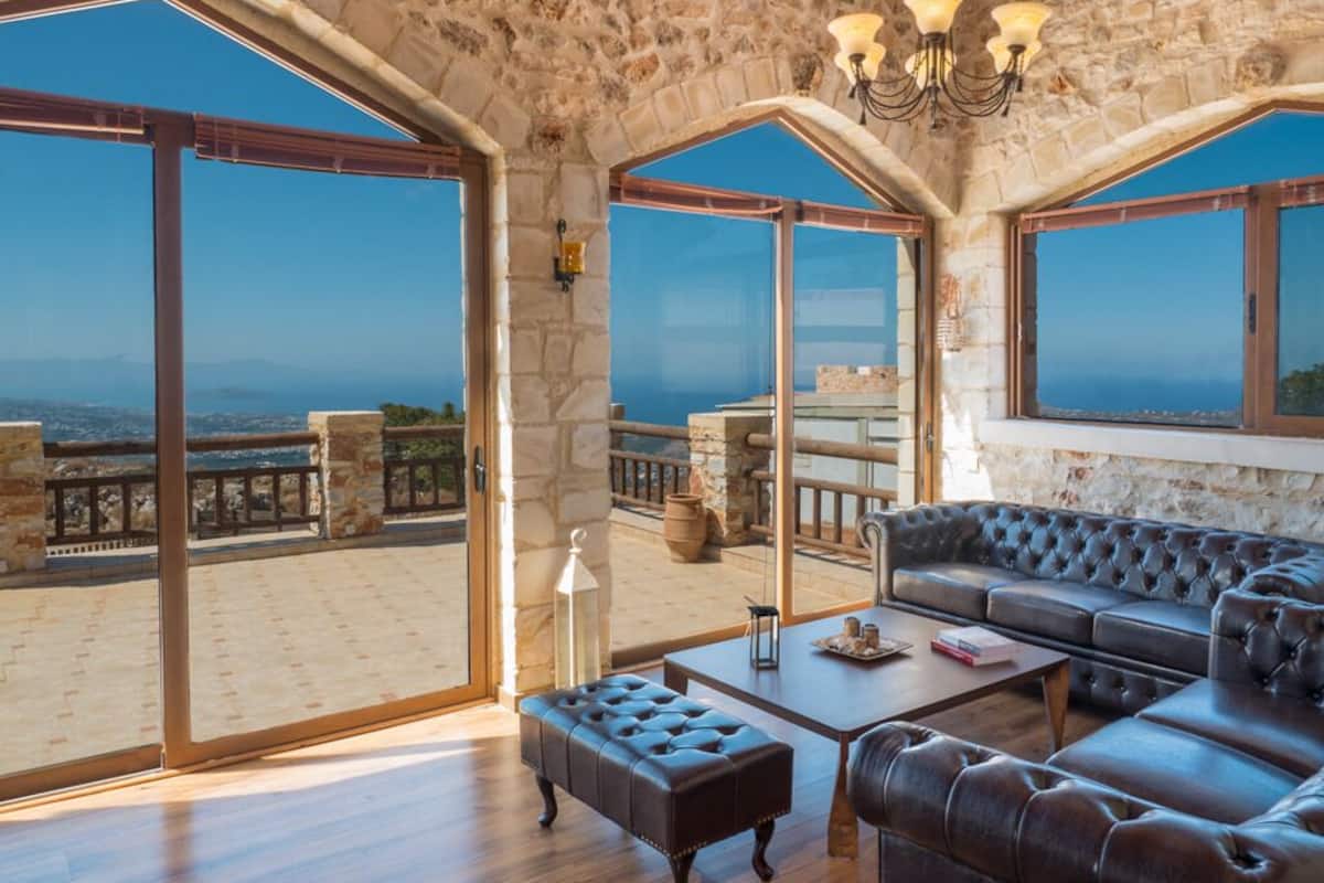 A spacious living area with a stone ceiling, large windows offering a view of the sea, and a leather sofa.