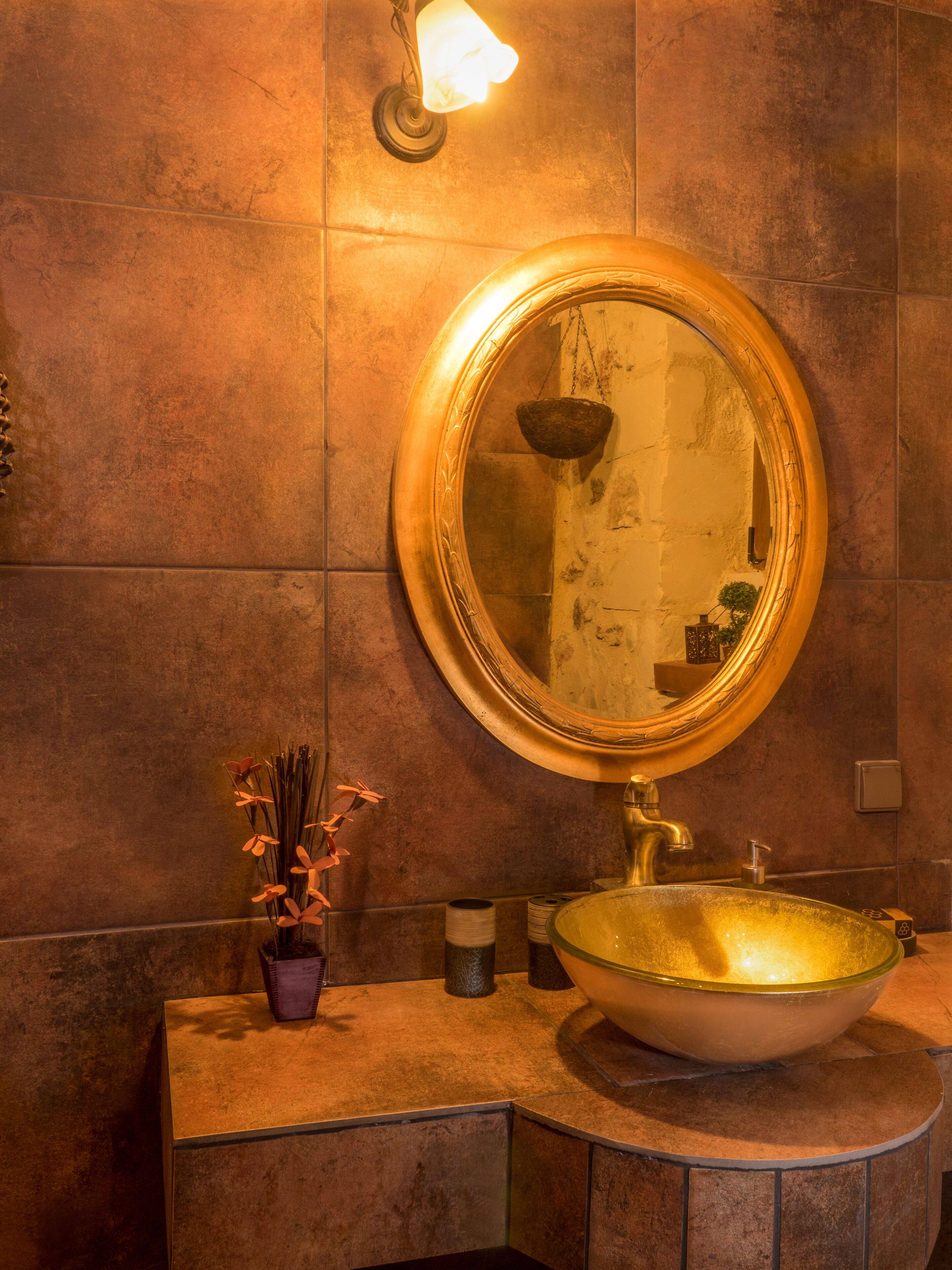 A bathroom with a round mirror, a vessel sink, and a wall-mounted light fixture.