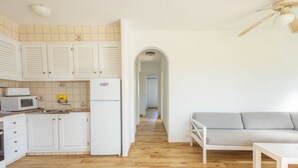 Een moderne keuken met witte kasten, een magnetron en een koelkast. De woonruimte heeft een houten vloer en een grijze bank.