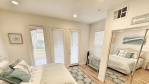 A bedroom with a large bed, a bedside table, a mirror, and a view of another room. - Coastal Condo - Gated, Pool, Spa, Walk To The Beach (Huntington Beach)