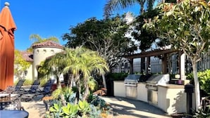 An outdoor patio with a barbecue grill, lounge chairs, and a small garden area. - Coastal Condo - Gated, Pool, Spa, Walk To The Beach (Huntington Beach)