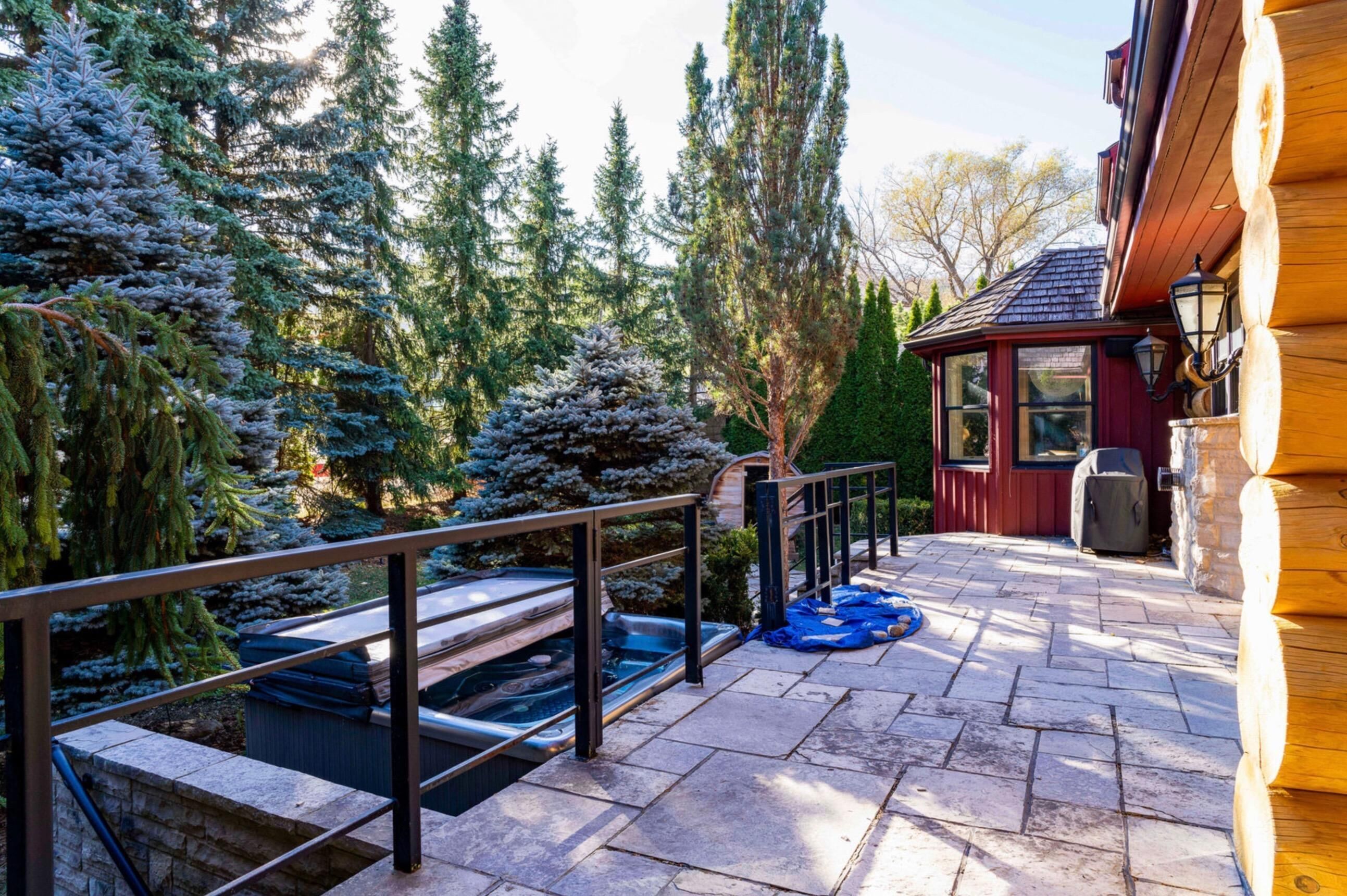 A stone patio with hot tubs, a wooden deck, and a view of evergreen trees.