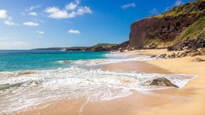 Een strand met helder turquoise water, een zandstrand en een rotsachtige klif.