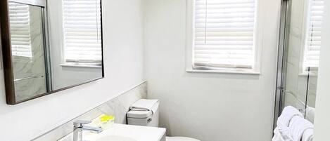 A modern bathroom with a white sink, toilet, and shower.