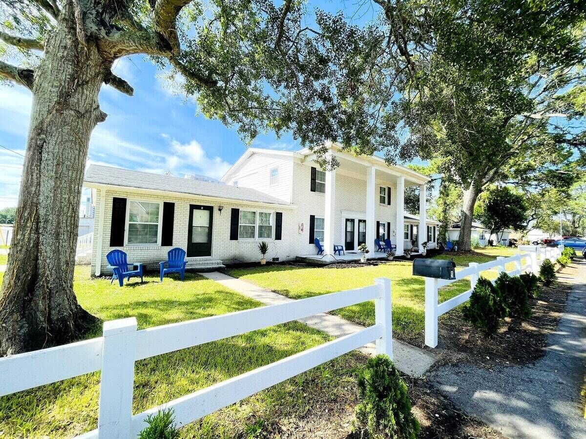 A white two-story house with a porch, blue chairs, and a white picket fence.