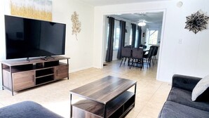 A modern living room with a flat-screen TV, dark wooden coffee table, grey sofa, and a dining area with chairs and a table. - Great duplex near the beach (North Myrtle Beach)