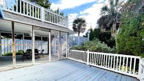 A covered outdoor deck with a white railing, a table with chairs, and a view of a house with a balcony. - Great duplex near the beach (North Myrtle Beach)