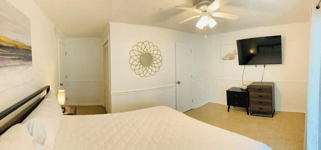 A bedroom with a bed, a ceiling fan, a TV, and a dresser.
