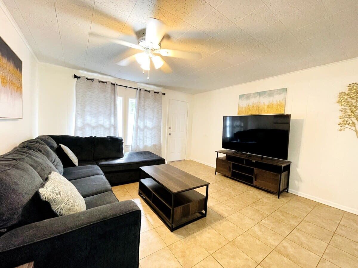 A living room with a black sofa, a coffee table, a TV on a stand, and a ceiling fan.