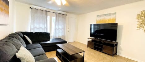 A living room with a black sofa, a coffee table, a TV on a stand, and a ceiling fan.