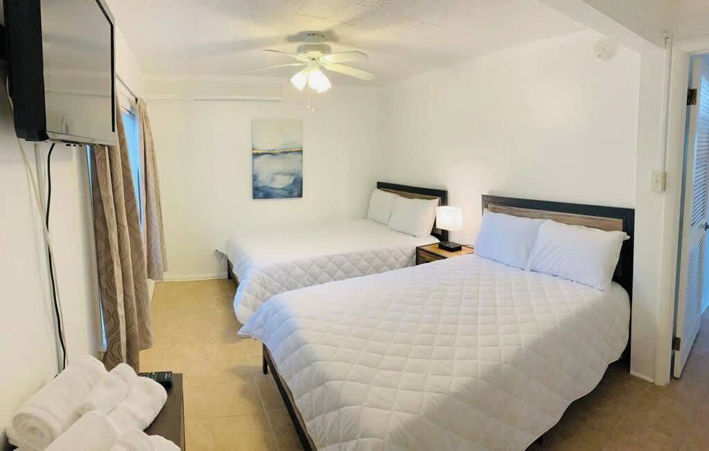Une chambre d’hôtel avec deux lits, un ventilateur de plafond, un téléviseur fixé au mur et un tableau accroché au mur.