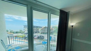 A balcony with a view of a swimming pool and buildings, a chair, a lamp, and a vent. - Coastal Retreat at Carolina Winds #2 + Pool (Myrtle Beach)