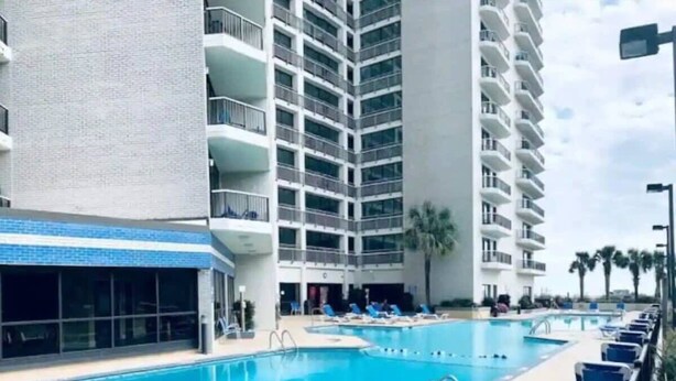 A swimming pool with lounge chairs, a building with balconies, and a clear sky. - Coastal Retreat at Carolina Winds #2 + Pool (Myrtle Beach)