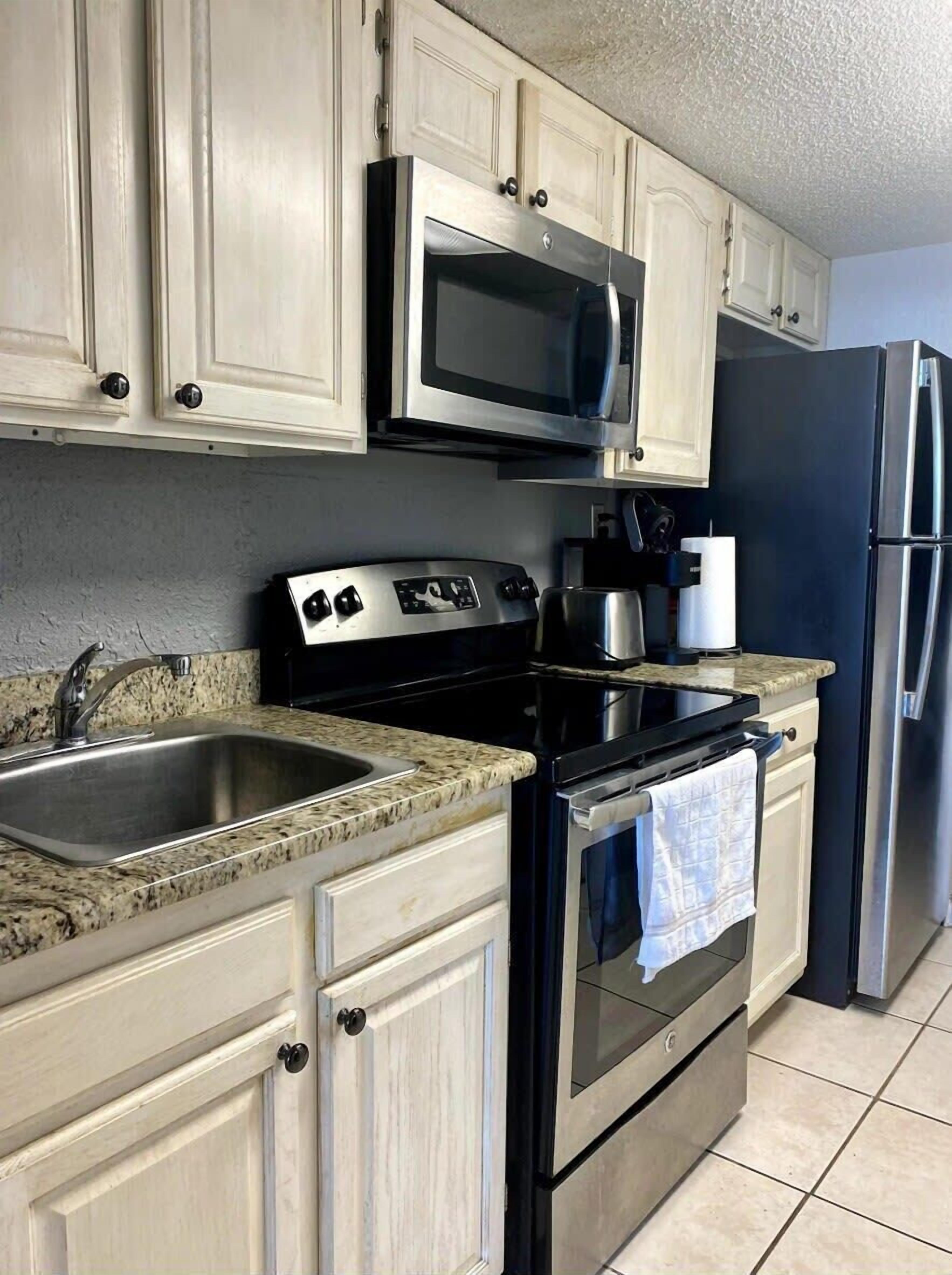 A kitchen with a stainless steel sink, a microwave, a stove, and a refrigerator.