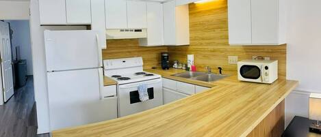 Una cocina moderna con armarios blancos, una encimera de madera, una estufa, un refrigerador y un microondas.