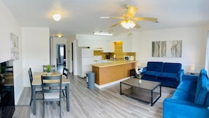 A modern living room with a blue sofa, wooden coffee table, and a dining area with a table and chairs.