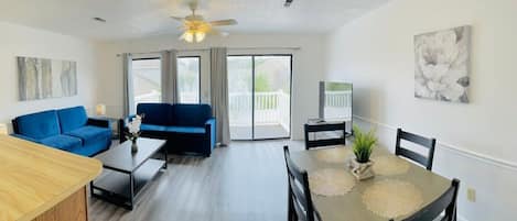 A modern living room with a blue sofa, a dining table with a placemat, and a ceiling fan.