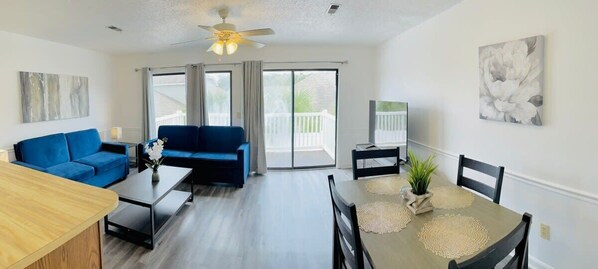A modern living room with a blue sofa, a dining table with a placemat, and a ceiling fan.