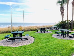 A coastal picnic area with tables and benches arranged on a paved surface, overlooking the sea.