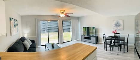 A spacious living area with a wooden dining table, a sofa, and a ceiling fan.